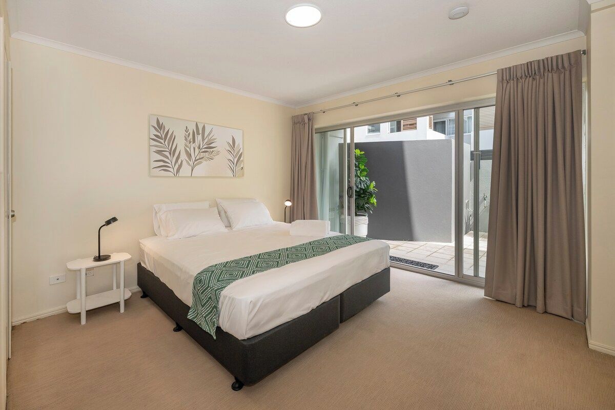 A bedroom with a bed, bedside table, and a view of a balcony.
