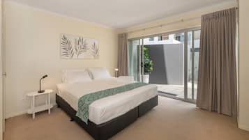 A bedroom with a bed, bedside table, and a view of a balcony.