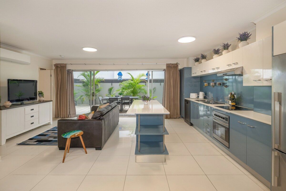 A modern kitchen with a central island, a dining area with a sofa, and a TV in the living room.