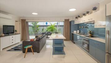 A modern kitchen with a central island, a dining area with a sofa, and a TV in the living room.