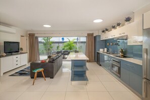 A modern kitchen with a central island, a dining area with a sofa, and a TV in the living room. - Huge terrace apartment (~150sqm) with free parking (Fortitude Valley)