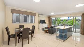 A modern living room with a dining area, a sofa, a TV, and a balcony with a view of greenery.