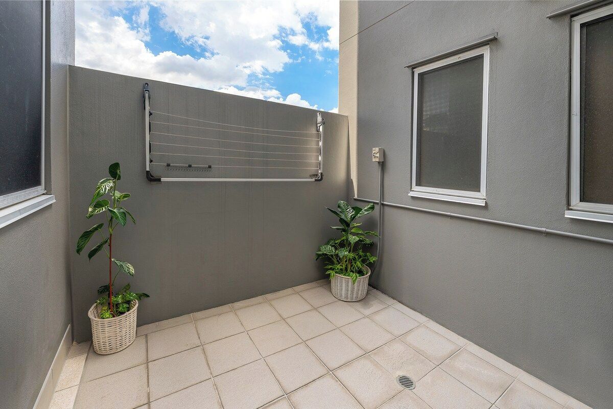 A small, enclosed outdoor area with a tiled floor, a metal drying rack, and two potted plants.