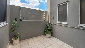 A small, enclosed outdoor area with a tiled floor, a metal drying rack, and two potted plants.