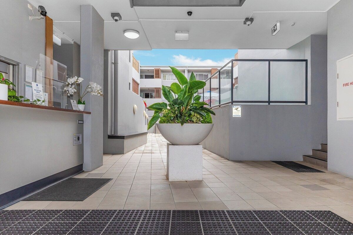 A reception area with a reception desk, potted plants, a large planter, and a staircase leading to an upper floor.