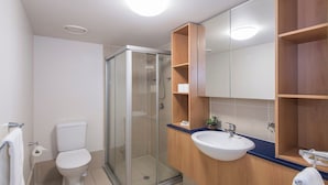 Ein modernes Badezimmer mit einer Duschkabine aus Glas, einer weißen Toilette, einem Holzbadezimmermöbel mit Waschbecken und einem großen Spiegel.
