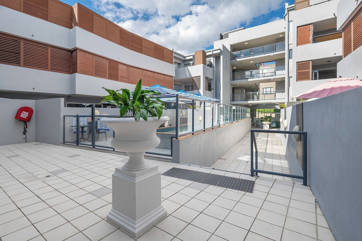 A modern outdoor area with a white tiled floor, a white column with a planter, and a blue and white striped awning.
