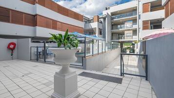 A modern outdoor area with a white tiled floor, a white column with a planter, and a blue and white striped awning.
