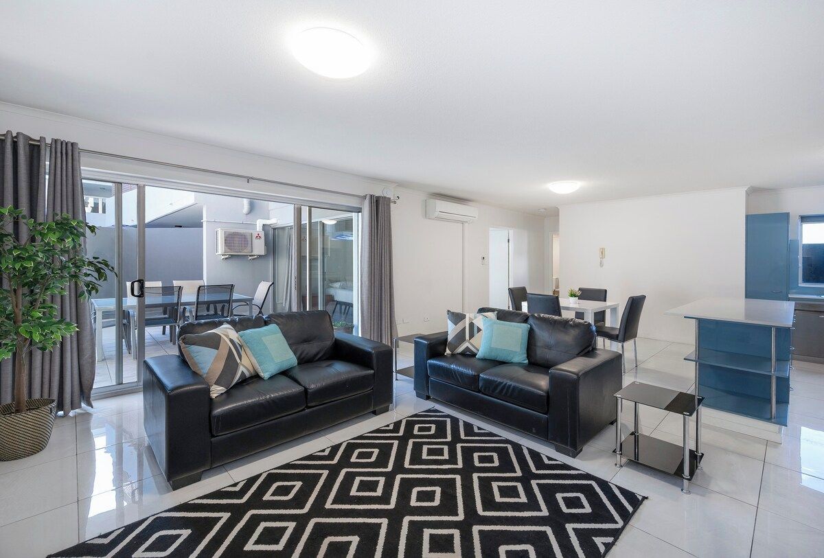 A modern living room with two black leather sofas, a glass coffee table, and a patterned rug.