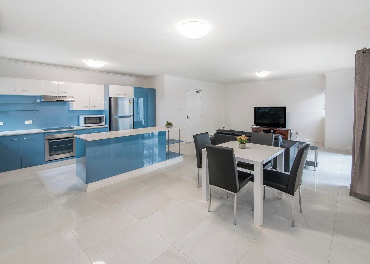 A modern kitchen with blue cabinets, a central island, and a dining area with a table and chairs.