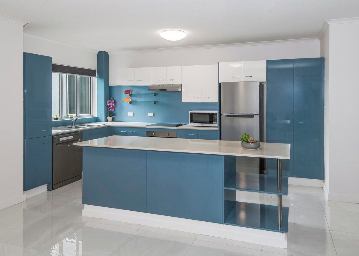 A modern kitchen with a central island, stainless steel appliances, and blue cabinetry.