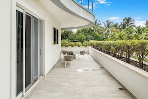 A balcony with a curved ceiling, sliding glass doors, and a seating area with chairs. - Condo at ONE Cable Beach with Infinity Pool (Nassau)