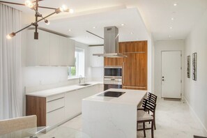 A modern kitchen with a central island, built-in appliances, and a dining area with chairs. - Condo at ONE Cable Beach with Infinity Pool (Nassau)
