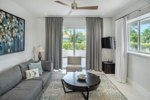A modern living room with a sofa, a coffee table, a television, and a ceiling fan. - Condo at ONE Cable Beach with Infinity Pool (Nassau)
