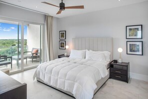Une chambre avec un grand lit, un ventilateur de plafond, une table de chevet et une vue sur un balcon.