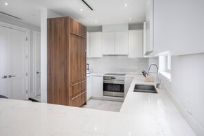 A modern kitchen with white cabinetry, a wooden cabinet, stainless steel appliances, and a marble countertop. - One bedroom condo at ONE Cable Beach (Nassau)
