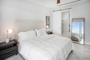 A modern bedroom with a large bed, a bedside table with a lamp, and a large mirror reflecting the room. - One bedroom condo at ONE Cable Beach (Nassau)