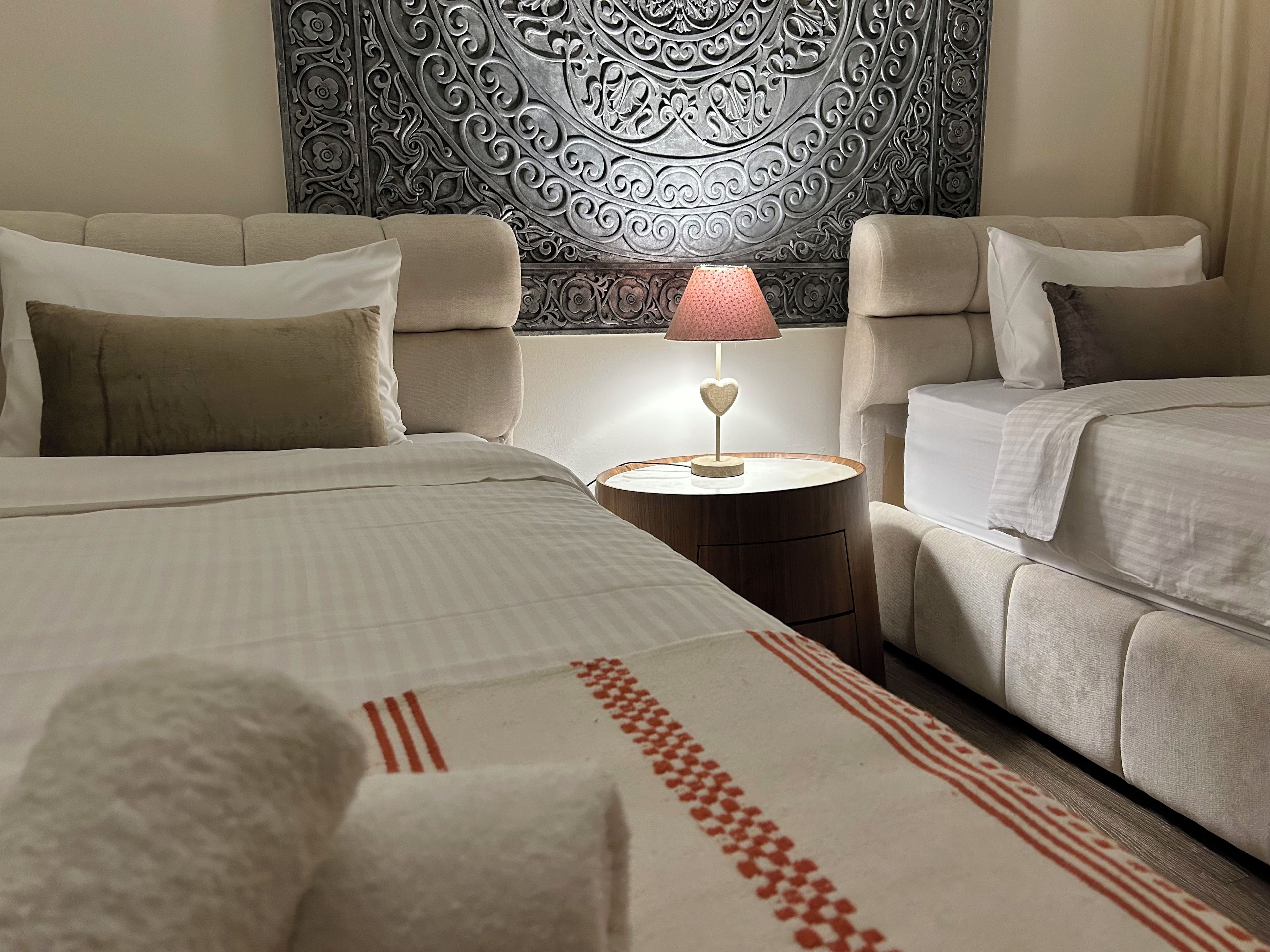 A hotel room with two beds, a decorative wall, and a bedside lamp.