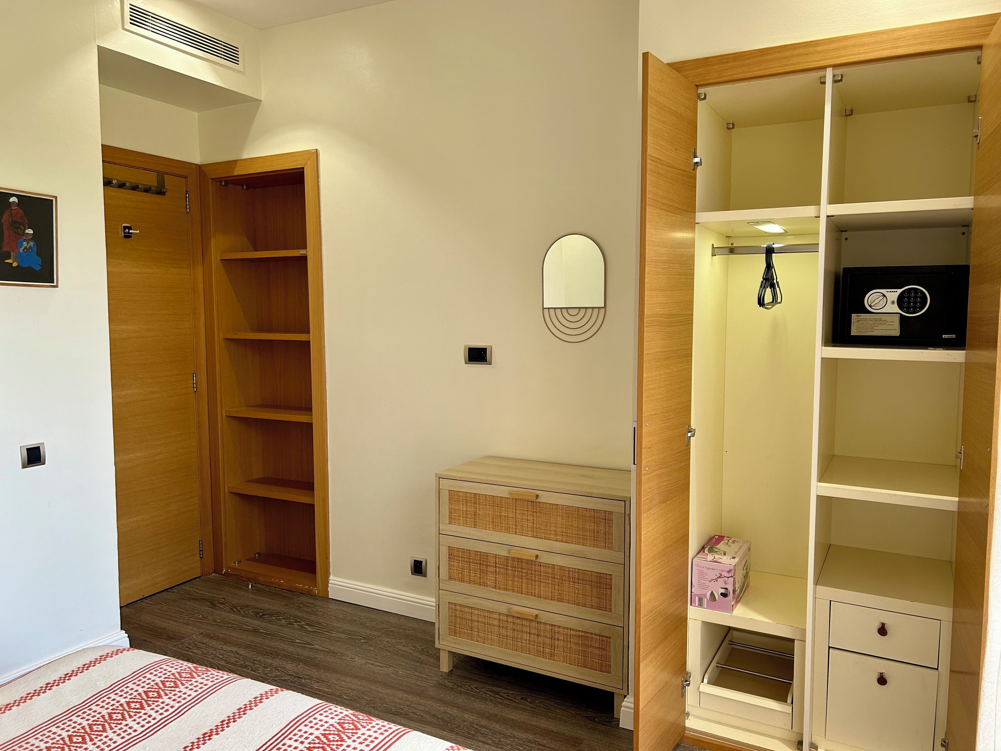 Une chambre à coucher avec une armoire en bois, une table de chevet, un miroir et un petit meuble.