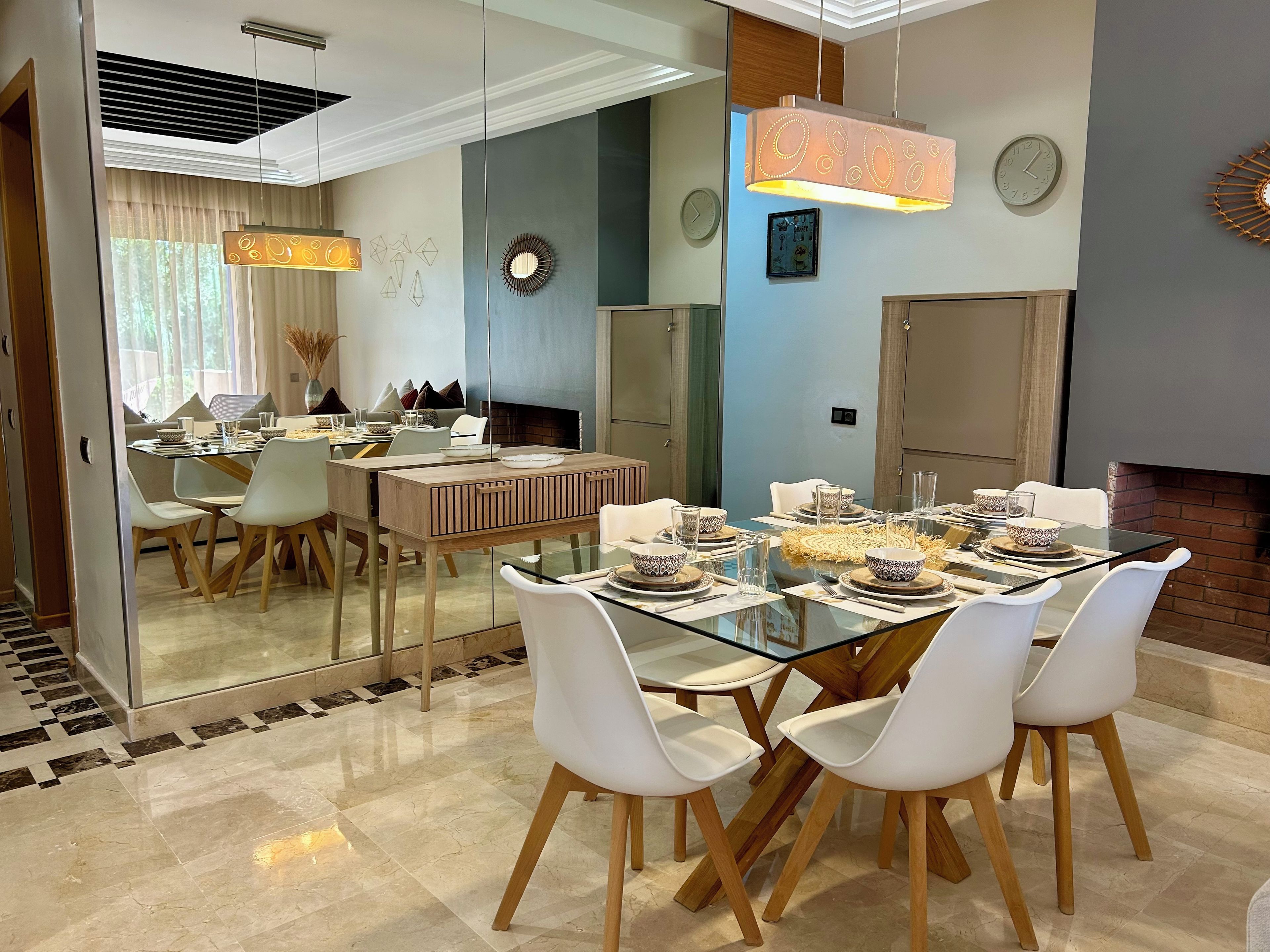 Un espace repas moderne avec une table en verre, des chaises blanches et une cheminée en briques.