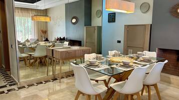 Un espace repas moderne avec une table en verre, des chaises blanches et une cheminée en briques.