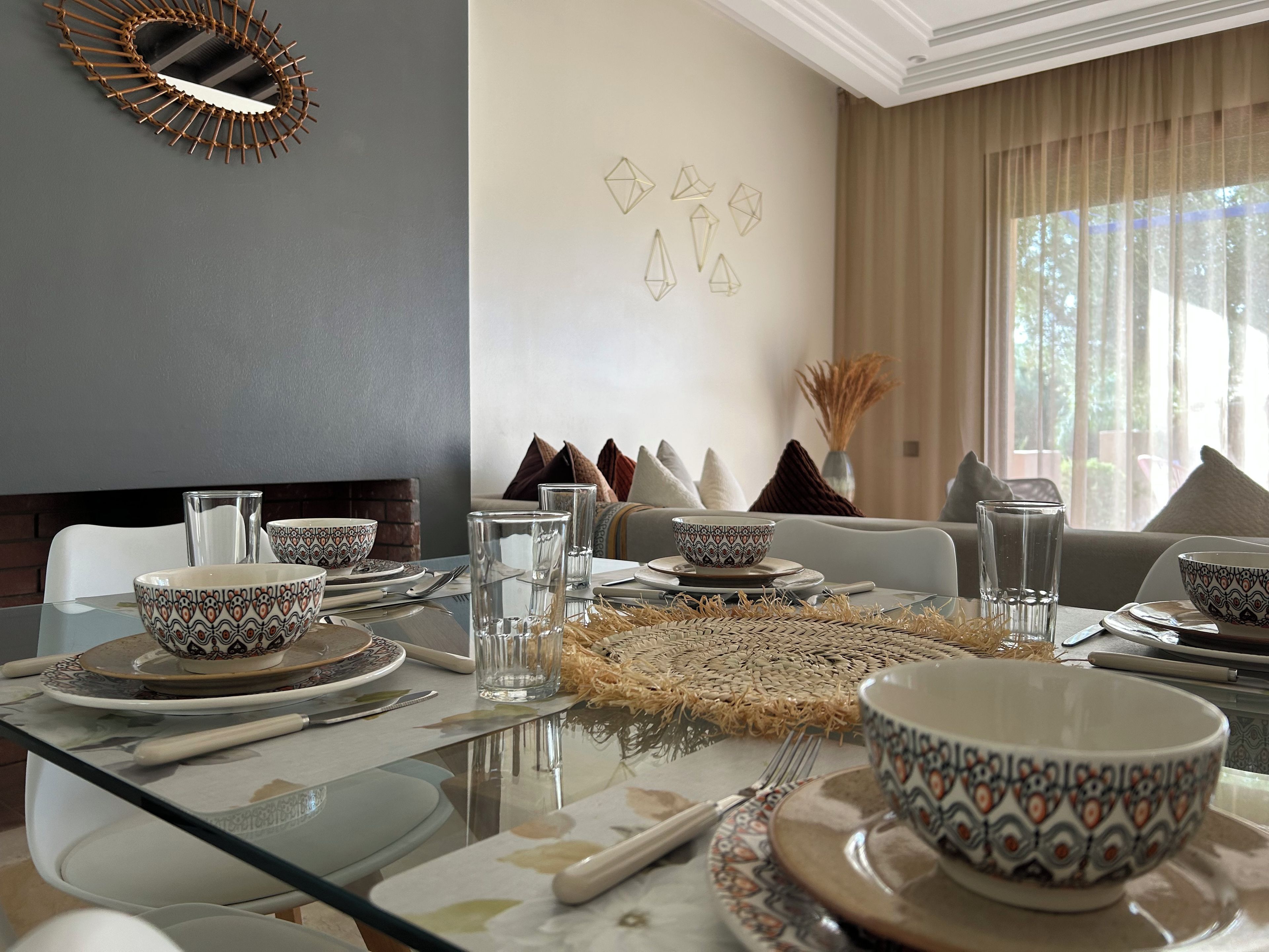 A dining area with a glass table set for a meal, including bowls, glasses, and cutlery.