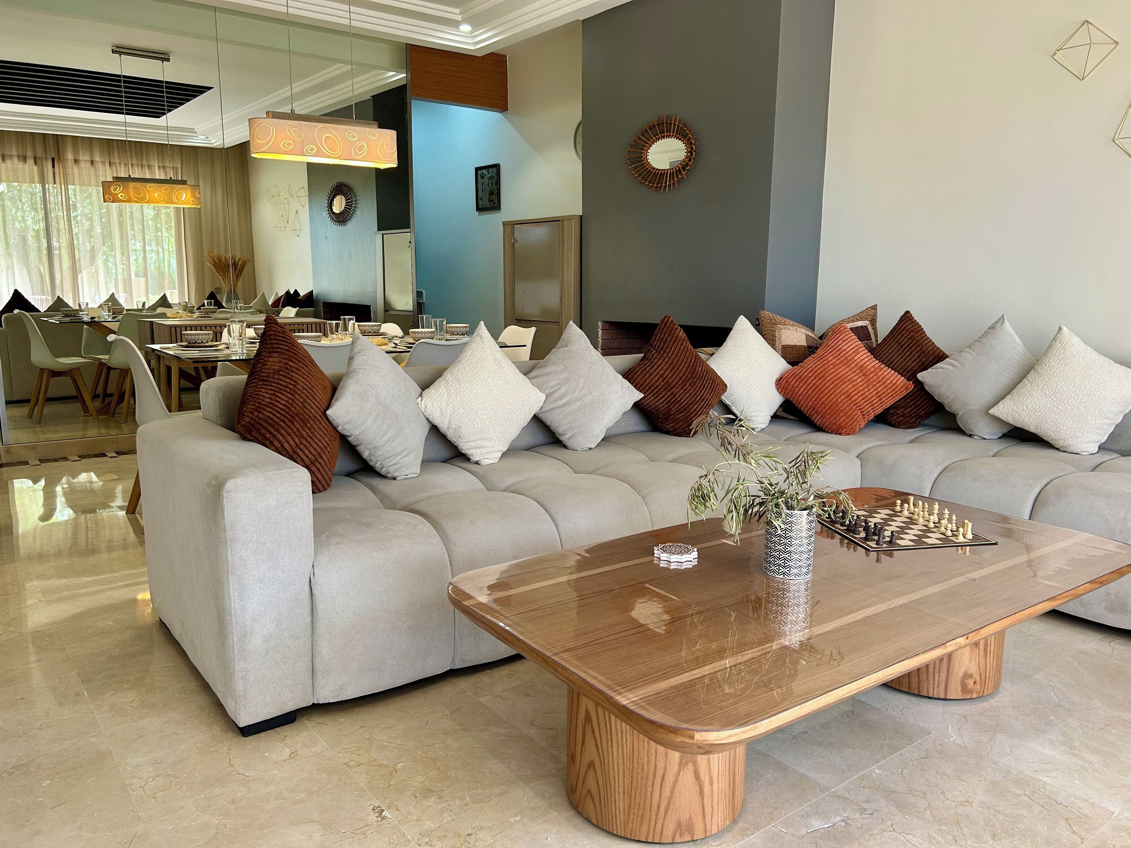 A modern living room with a sectional sofa, a wooden coffee table, and a dining area in the background.