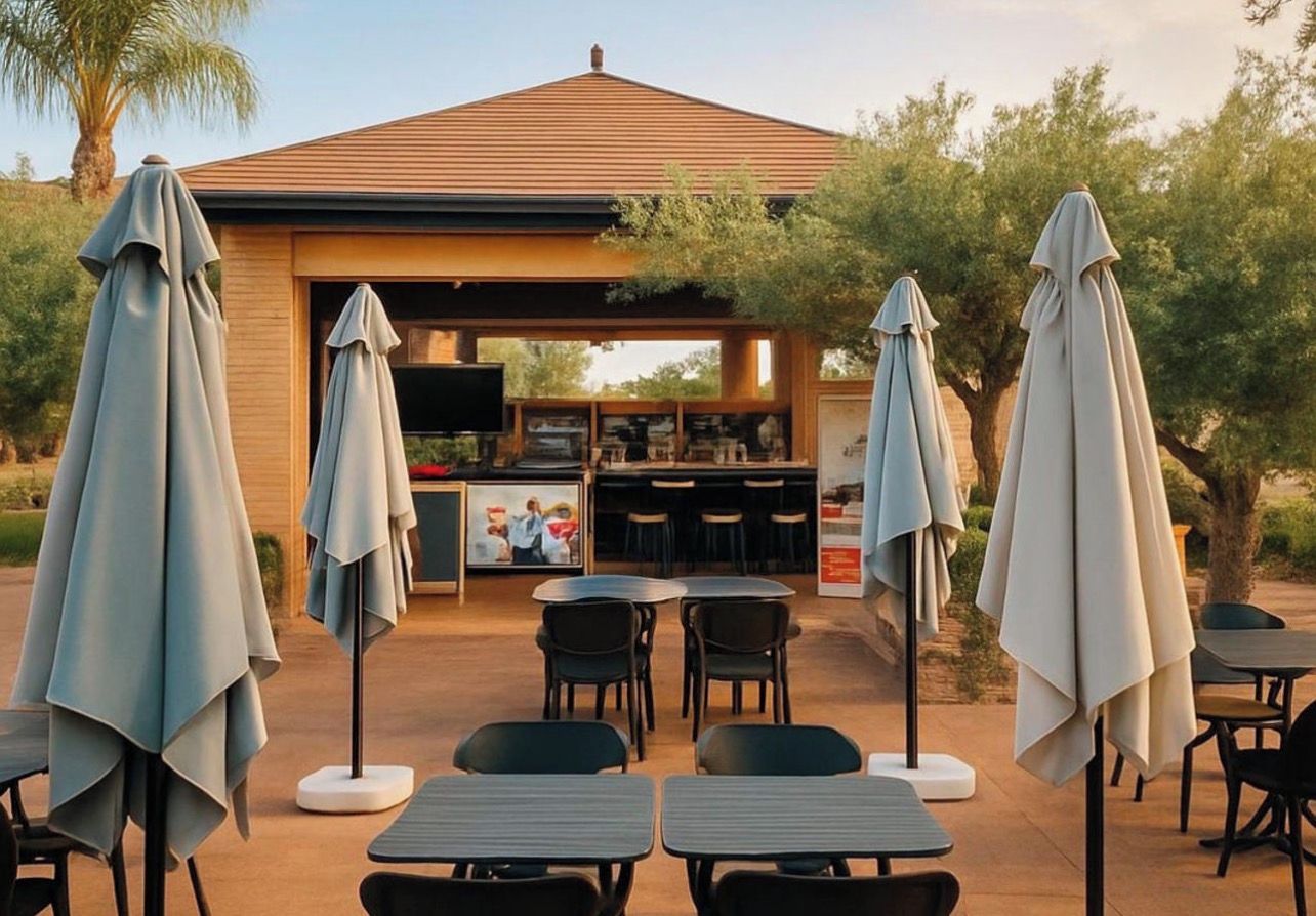 An outdoor dining area with tables and chairs, umbrellas, and a bar with a television.