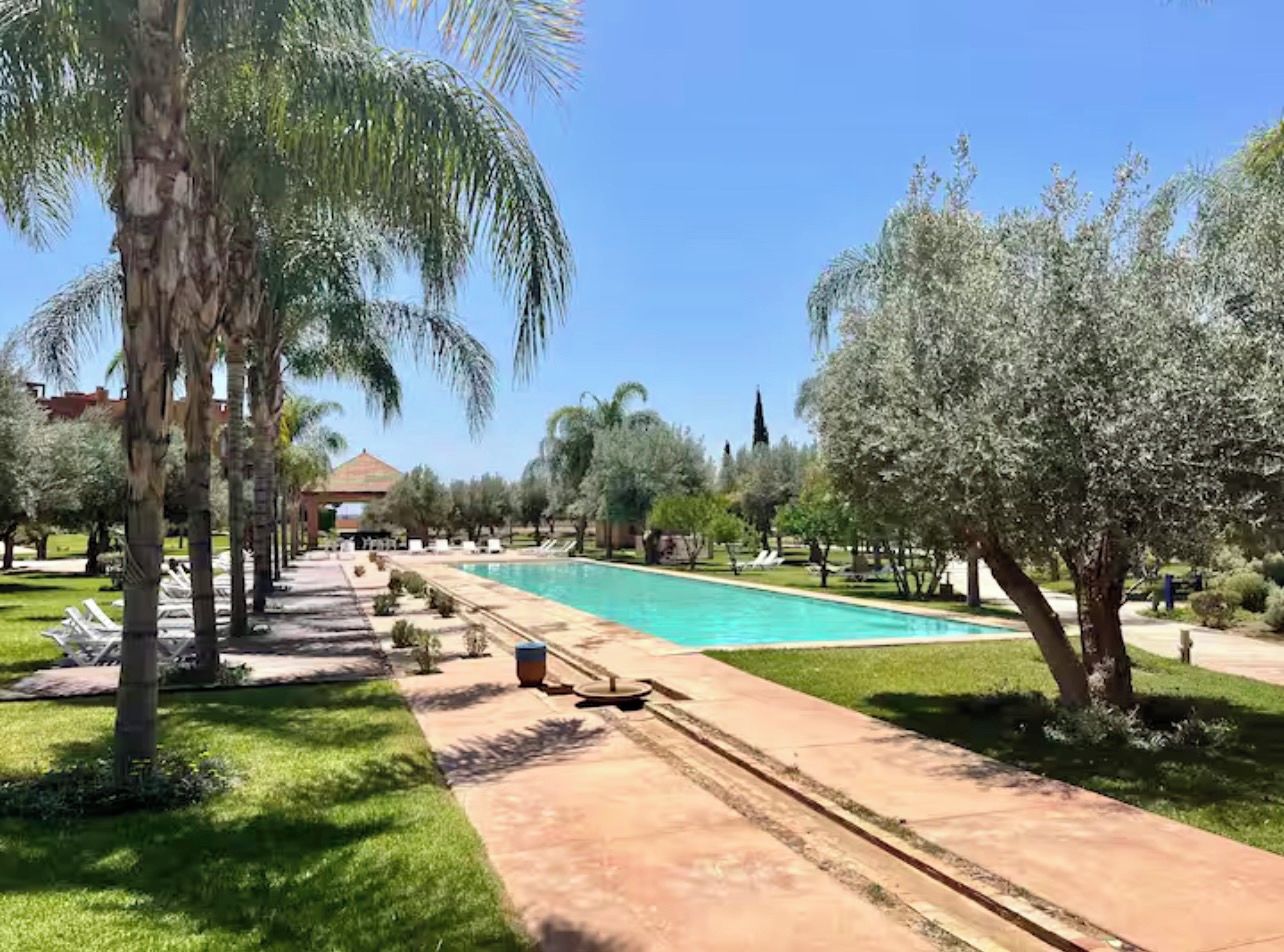 Un área de piscina con sillones de descanso y palmeras.