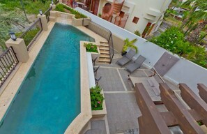 A rooftop pool with a clear blue water feature, surrounded by a low stone wall and metal railings. There are lounge chairs and a small seating area with a table and chairs. - Marbella lane - Chic Casa with Amazing OceanViews (Cabo San Lucas)