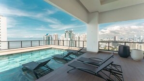 Ein Pool mit Überlauf und Stadtblick, ausgestattet mit Liegestühlen.