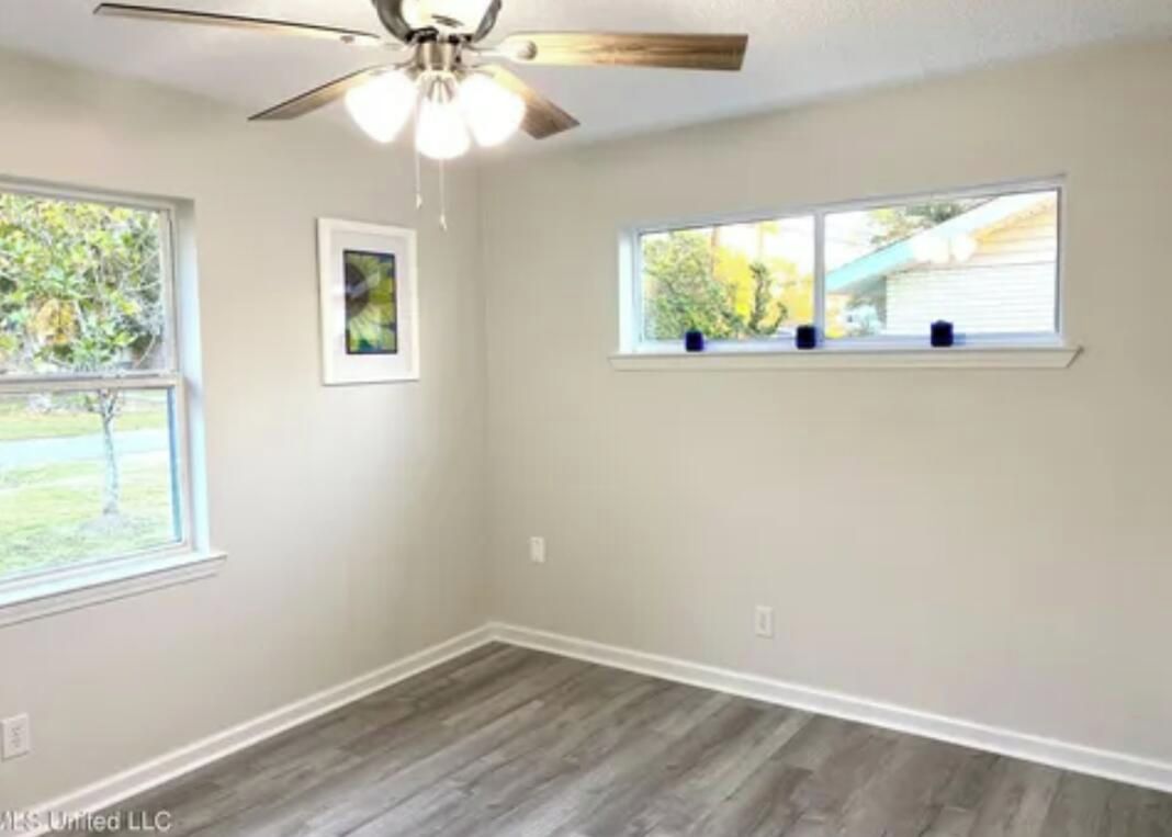 A room with a ceiling fan, two windows, and a wooden floor.