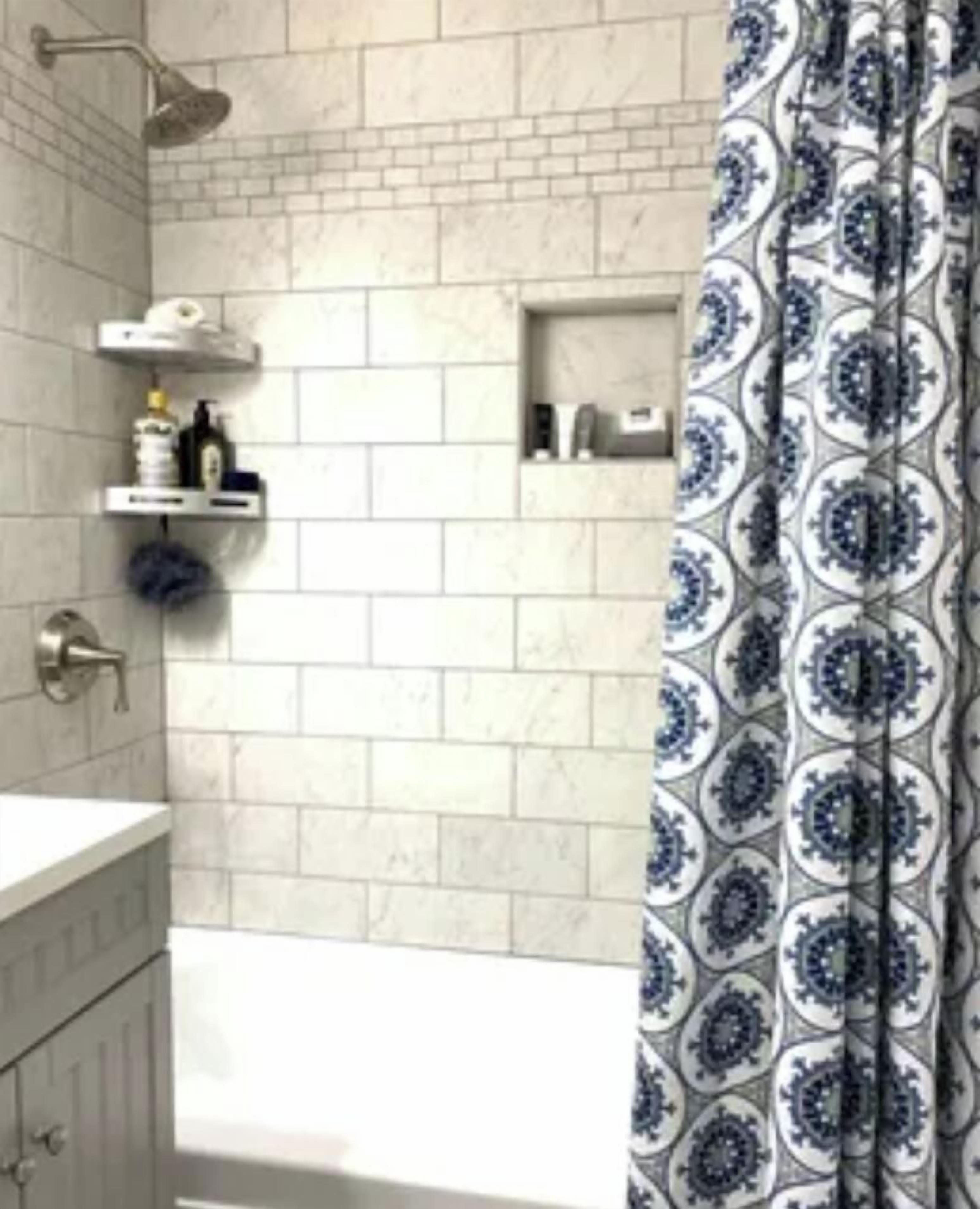 Een badkamer met een witte betegelde muur, een douche, een wit wastafelmeubel en een douchegordijn met een patroon.