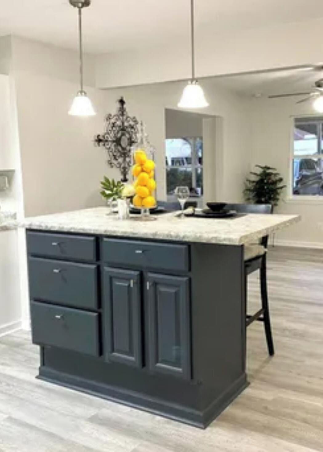 A kitchen with a large island, dark cabinetry, pendant lighting, and a potted plant.