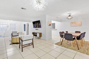 A modern living room with a dining area, a TV mounted on the wall, and a large window with sheer curtains. - 3-bedroom Lake house in Pembroke Pines/Miami (Pembroke Pines)