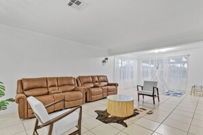 A modern living room with a brown leather sectional sofa, a white armchair, a round wooden coffee table, and a small white chair. - 3-bedroom Lake house in Pembroke Pines/Miami (Pembroke Pines)