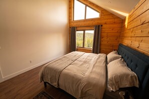 Une chambre avec un plafond en bois, une grande fenêtre avec des rideaux, un lit avec une literie beige et une tête de lit bleue.