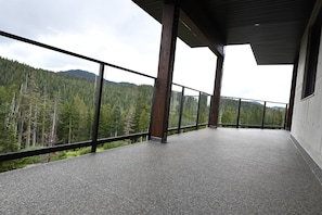 A balcony with a view of a forested mountain range. - Sabre Tooth Lodge - Luxury Stay on Mt. Washington. Hot Tub, Sauna, on site (Mt. Washington, Comox Valley)