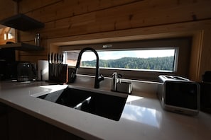 A kitchen with a sink, a window with a view of a forest, and a toaster. - Sabre Tooth Lodge - Luxury Stay on Mt. Washington. Hot Tub, Sauna, on site (Mt. Washington, Comox Valley)