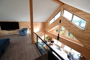 Ein geräumiges Loft-Zimmer mit großem Fernseher, einem blauen Sessel und einer Essecke mit Tisch und Stühlen.