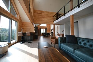 A spacious living area with a high ceiling, wooden beams, a dining area, and a view of the outdoors. - Sabre Tooth Lodge - Luxury Stay on Mt. Washington. Hot Tub, Sauna, on site (Mt. Washington, Comox Valley)