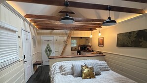 Quarto com uma cama grande, vigas de madeira, um claraboia e vista para a cozinha.