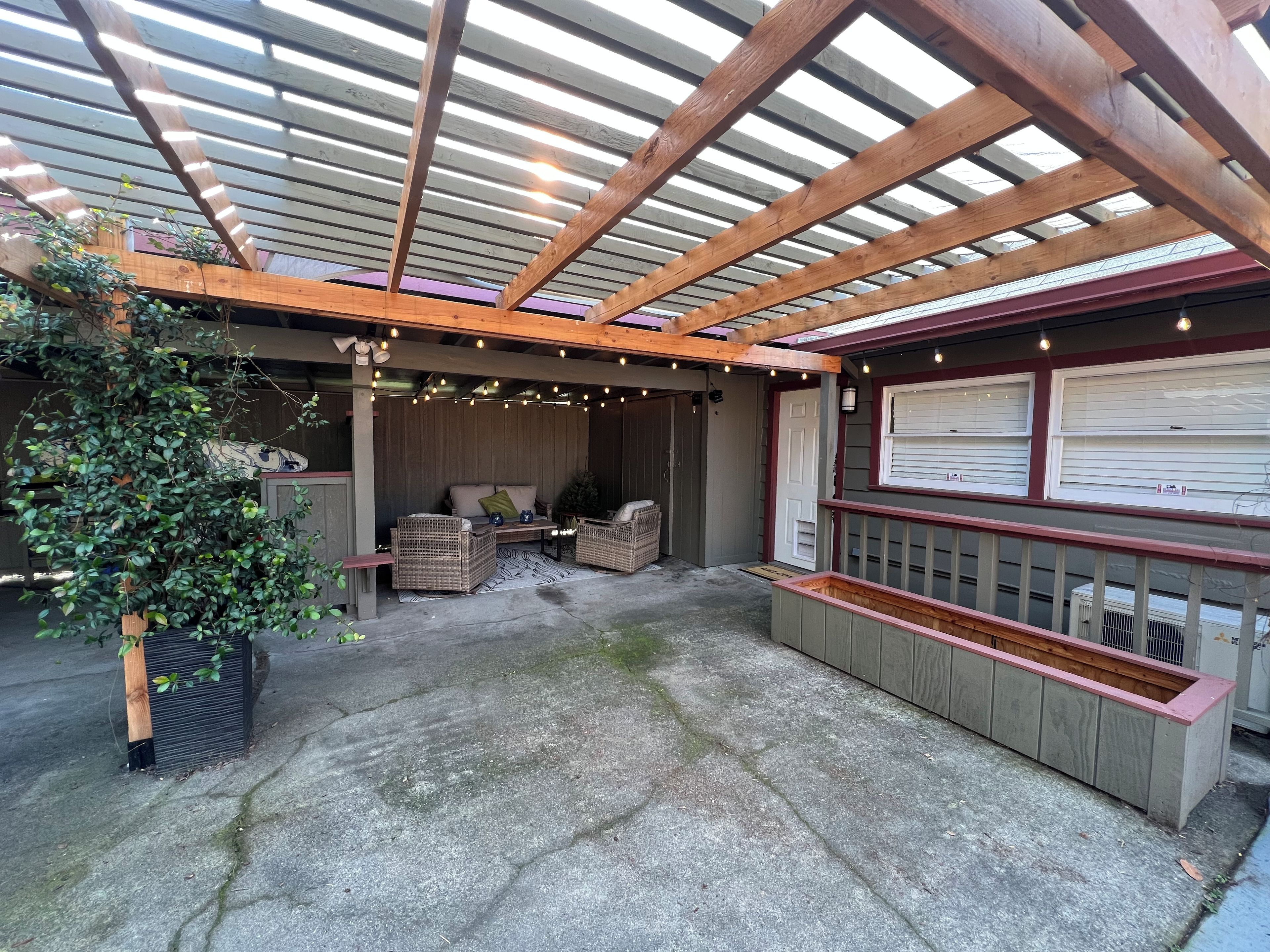 An outdoor patio with a wooden pergola, wicker furniture, and a built-in planter.