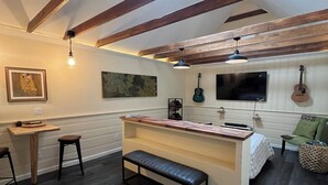 Quarto com teto de madeira, um banco, uma pequena mesa e uma cadeira verde.