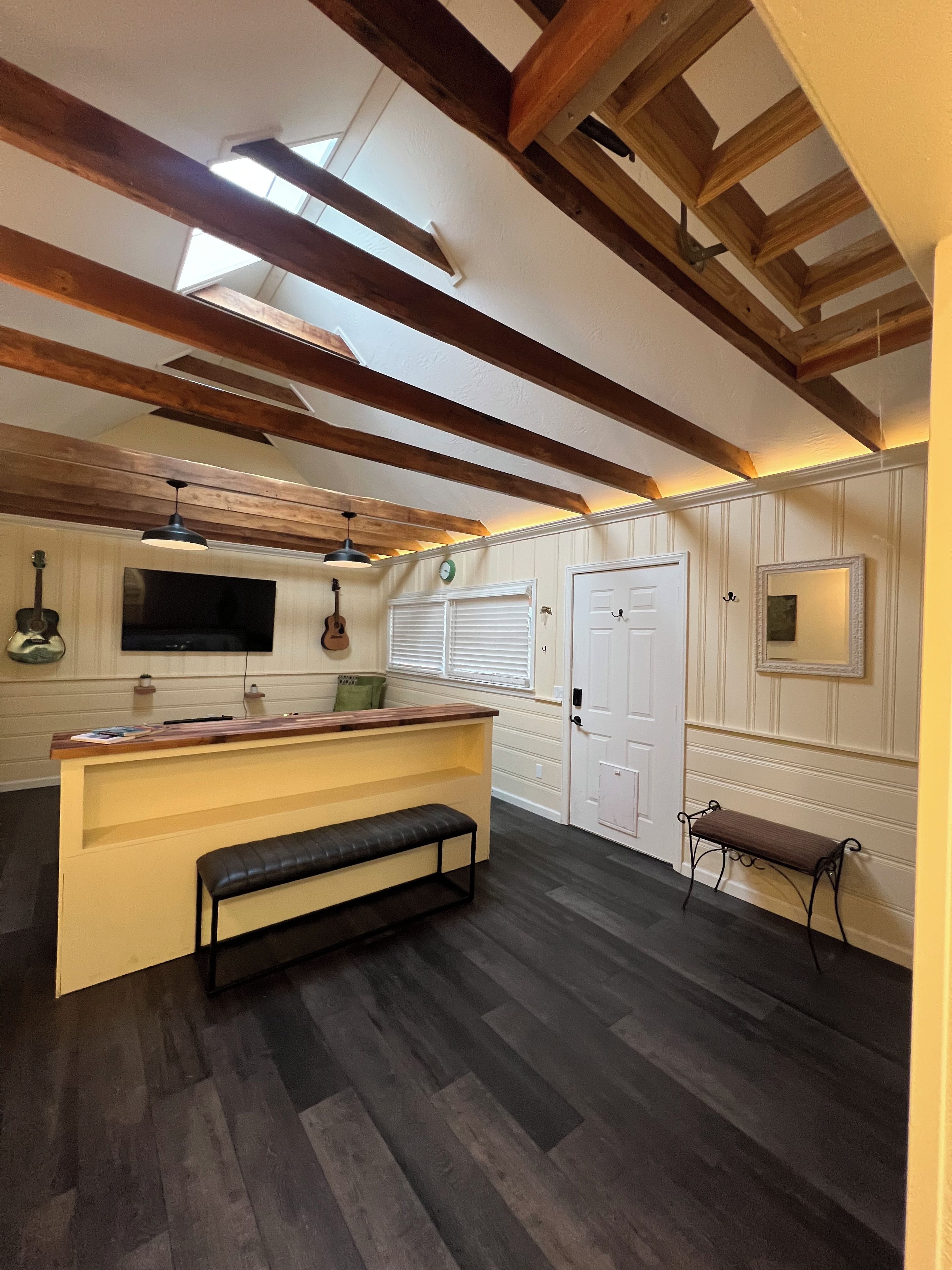 A room with a wooden ceiling, a bench, a small table, a door, and a wall-mounted TV.