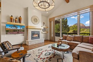 A spacious living room with a fireplace, a large window offering a mountain view, and a cozy seating area. - House of The Rising Sun - Hot Tub, Views, Forest (Sedona)
