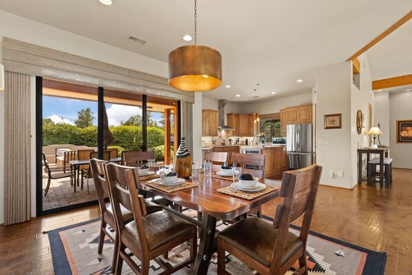 A spacious dining area with a large wooden table, chairs, and a hanging light fixture. - House of The Rising Sun - Hot Tub, Views, Forest (Sedona)