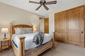 A bedroom with a wooden bed, a ceiling fan, a nightstand, and a large wooden door. - House of The Rising Sun - Hot Tub, Views, Forest (Sedona)