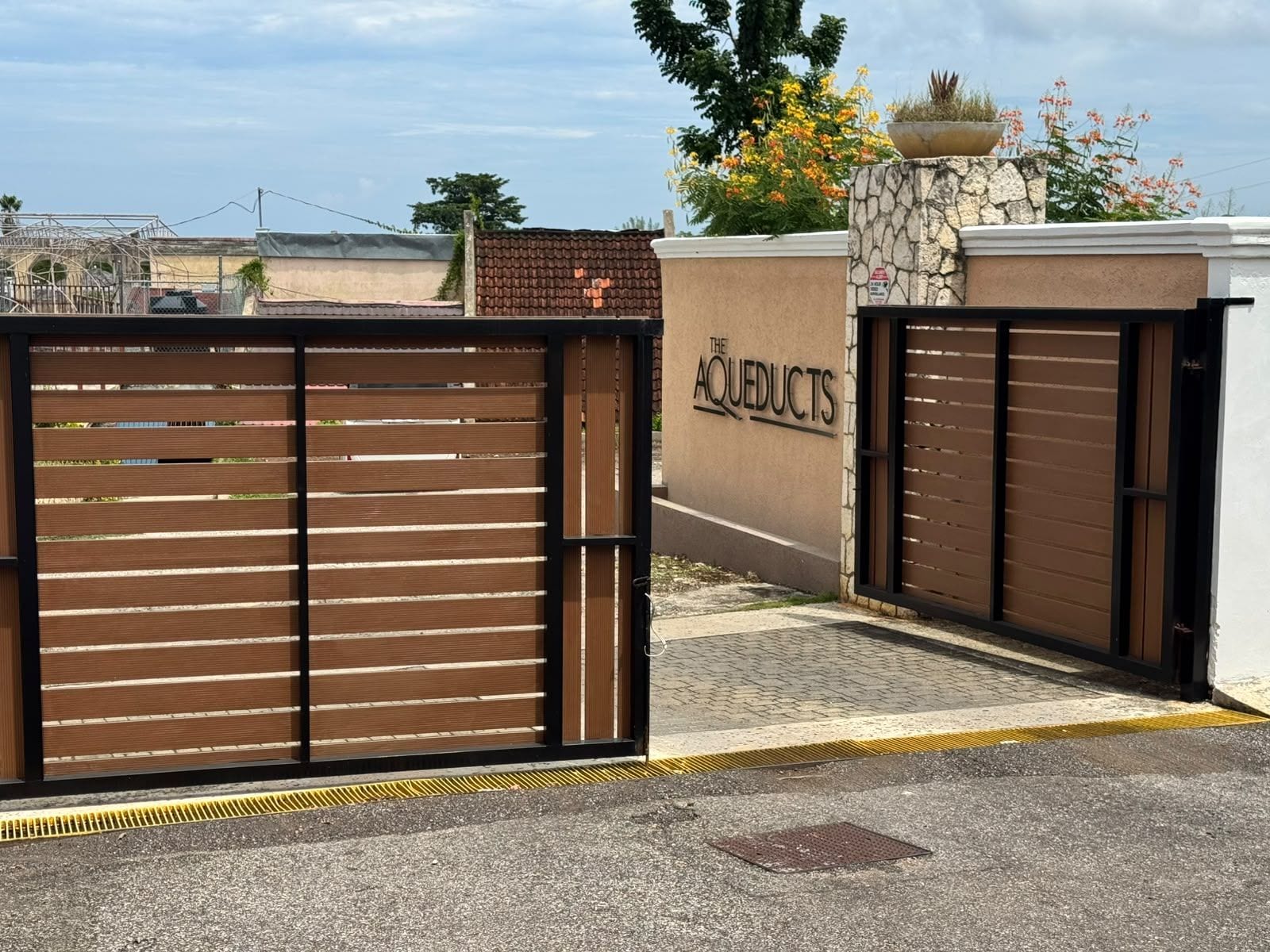 A gated entrance with a sign reading 'THE AQUEDUCTS' and a stone wall with a planter.
