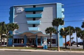 A hotel with a blue and white facade, palm trees in front, and a sign for 'Oasis Tikibar'. - Oceanfront Paradise at Fountain Beach Resort in gorgeous Daytona Beach (Daytona Beach Shores)